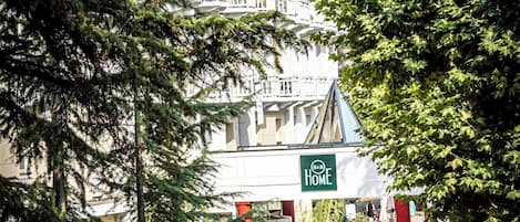 L’entrée d’un hôtel, avec une enseigne indiquant le mot « Accueil », est entourée d’arbres et offre une vue sur la montagne.