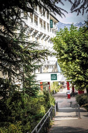A hotel entrance with a sign reading "Home," surrounded by trees and a mountain view. - B&B HOME Brides-Les-Bains Les 3 Vallées (Brides-les-Bains)