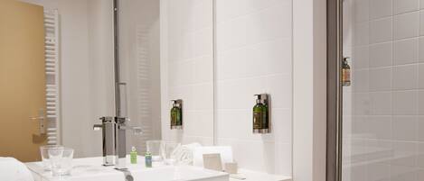 Un baño moderno con un espejo grande, lavamanos blanco y cabina de ducha con paredes de vidrio.