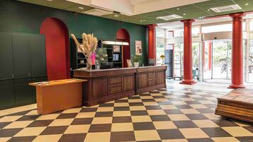 A reception area with a checkered floor, a reception desk, a green wall, and red columns.
