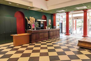 A reception area with a checkered floor, a reception desk, a green wall, and red columns. - B&B HOME Brides-Les-Bains Les 3 Vallées (Brides-les-Bains)