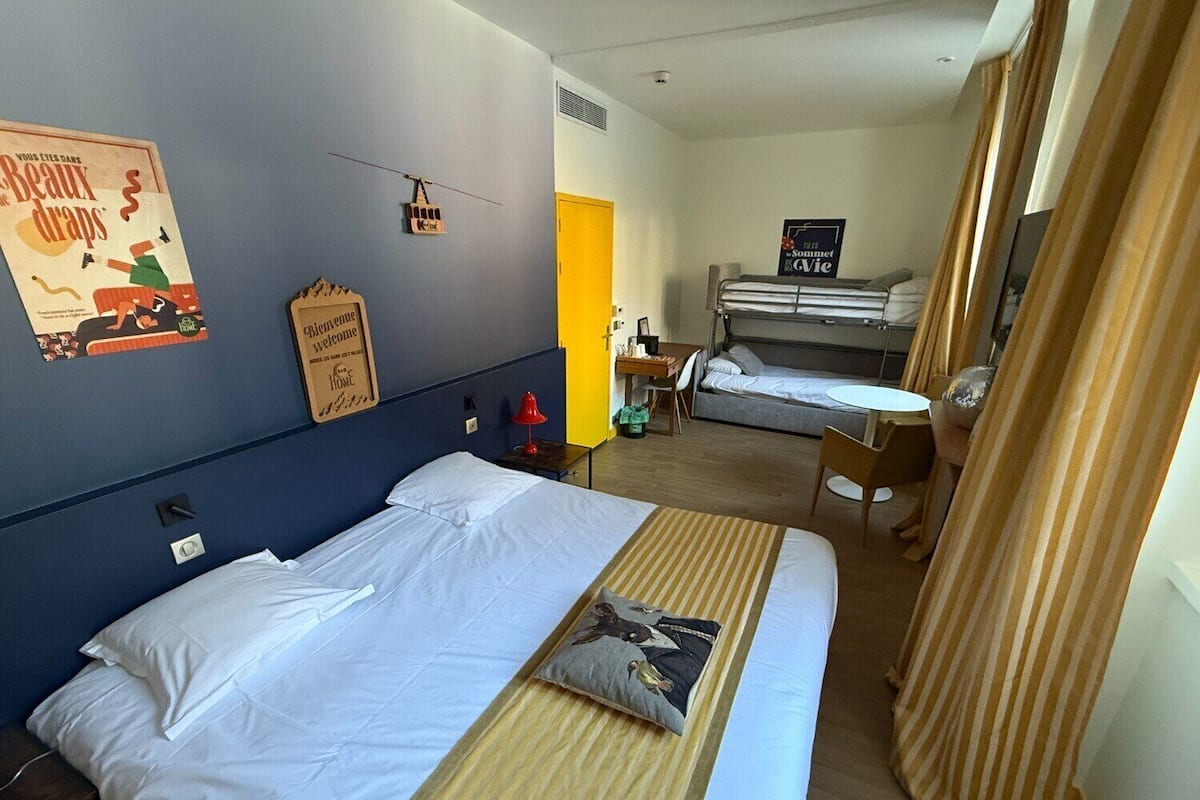 Habitación de hotel con dos camas, un escritorio y una silla. Hay un cartel en la pared y un letrero que dice "Welcome".