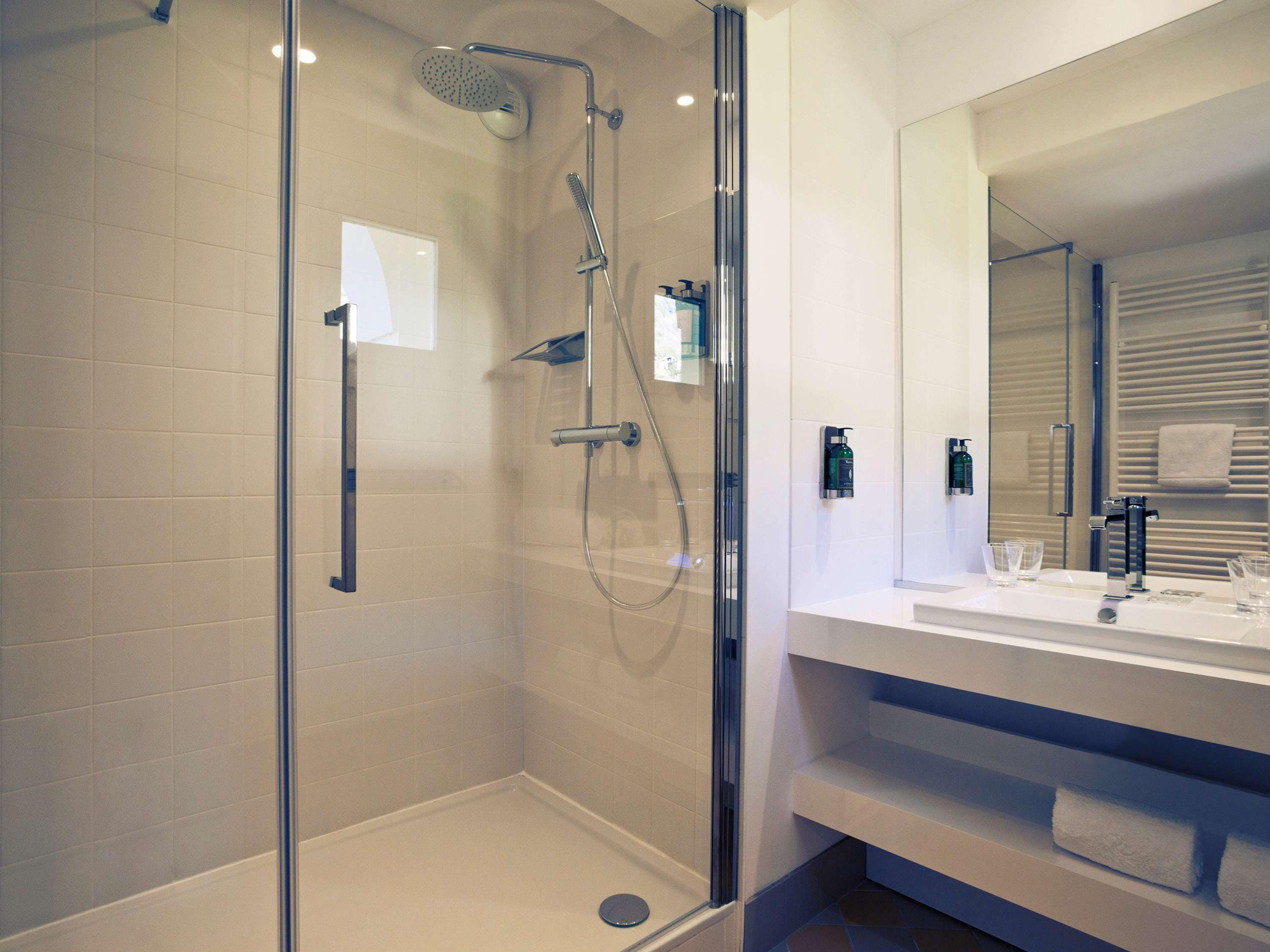 Un baño moderno con ducha envuelta en vidrio, un espejo grande y un tocador blanco con perchero.