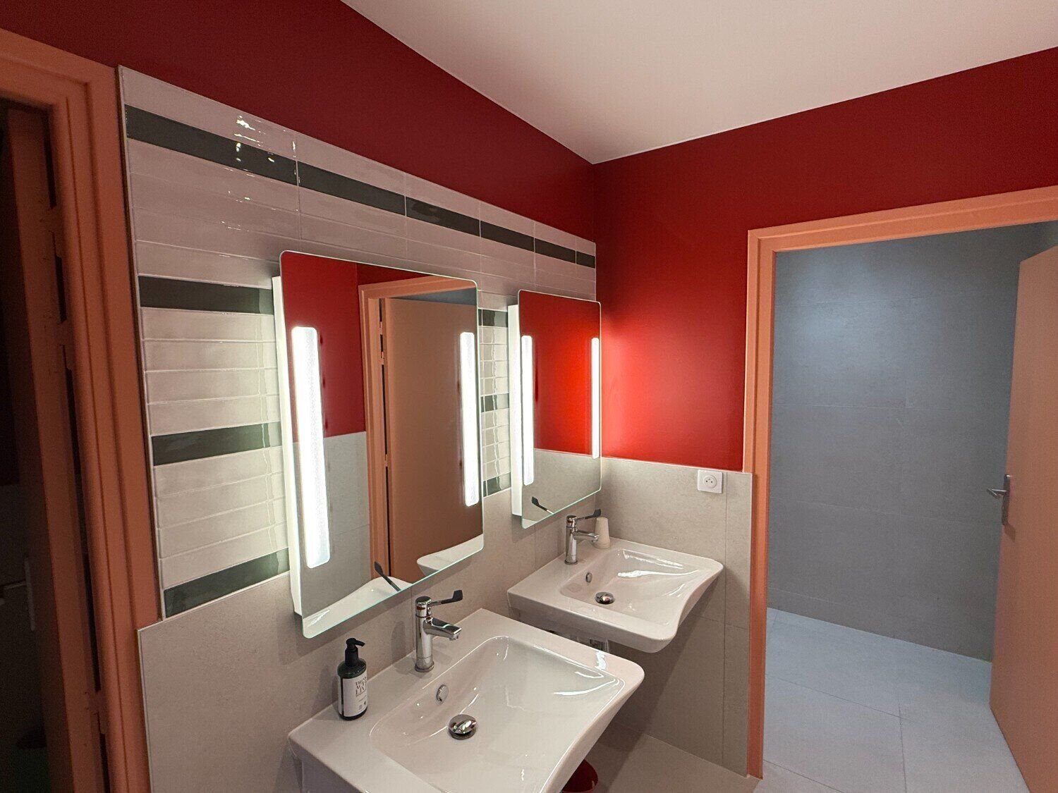 A bathroom with two sinks, a mirror, and a red wall.
