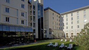 Un hotel con varios pisos, un área de estar al aire libre techada y un césped bien cuidado con sillones de descanso.