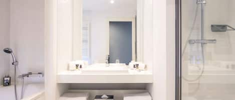 Un baño moderno con ducha acristalada, un espejo grande sobre un lavamanos blanco con dos toalleros y un suelo de baldosas con diseño.