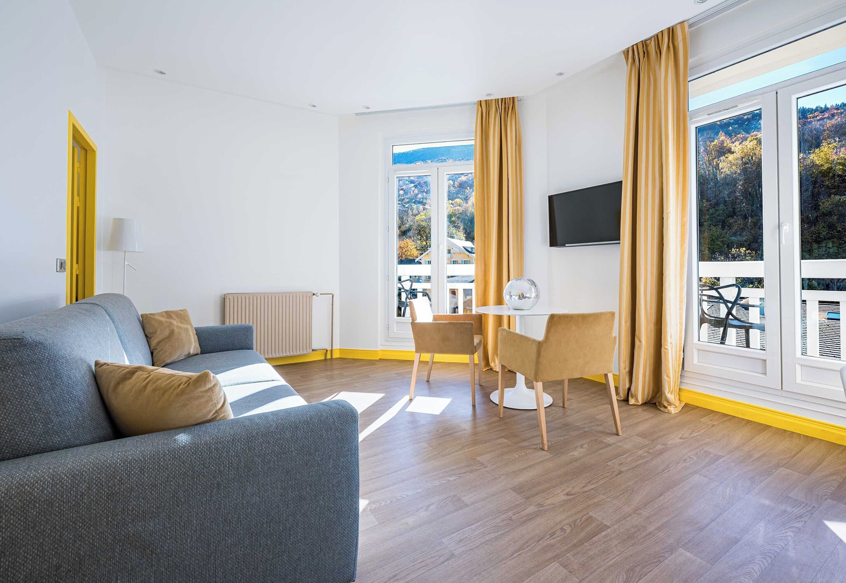 Una sala de estar moderna con un sofá, una mesa de comedor con sillas, un radiador y un televisor montado en la pared.