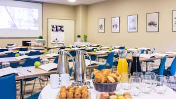 Un salón de conferencias con mesas dispuestas para una reunión, equipado con cafeteras, vasos de agua y un dispensador de jugo.