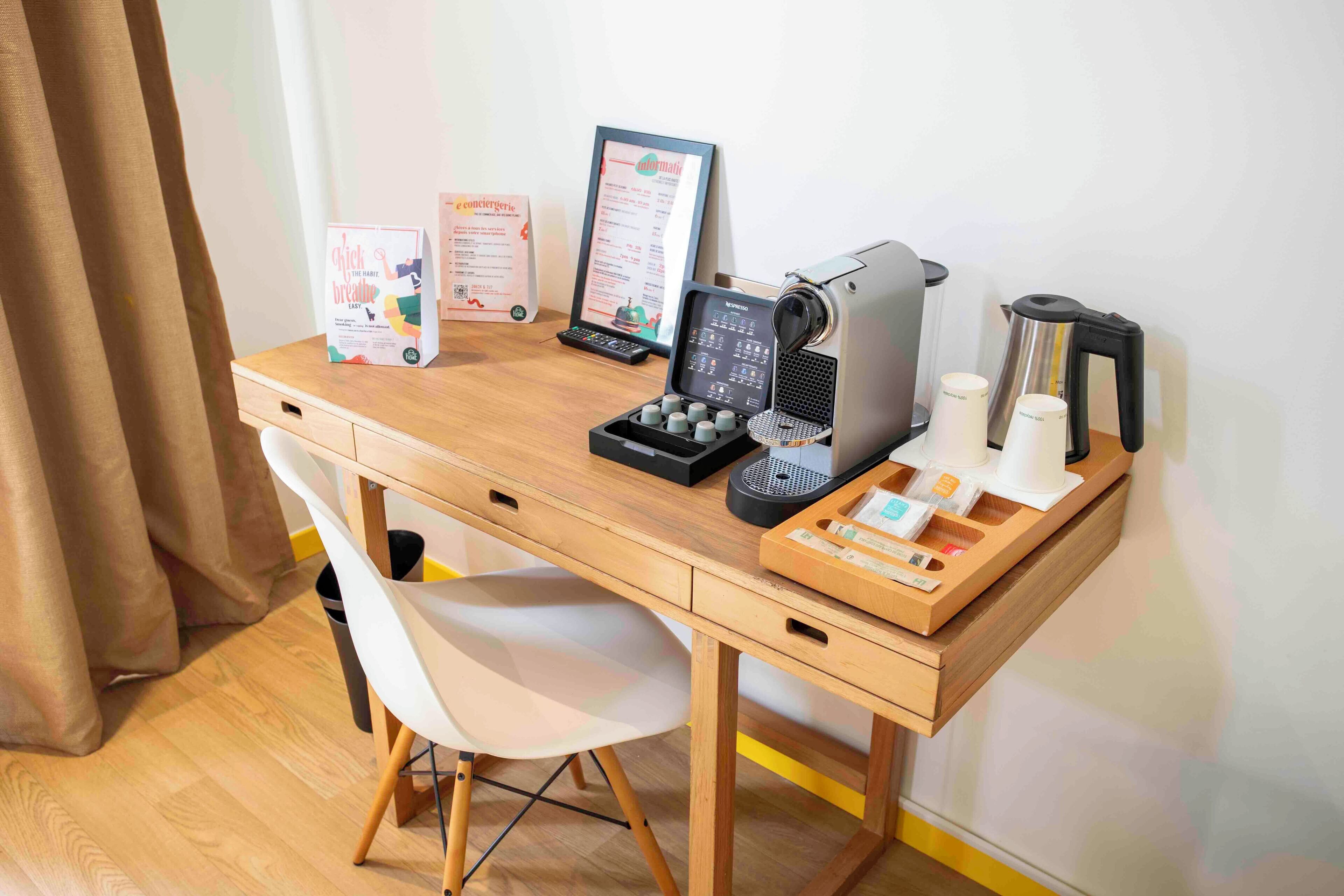 A wooden desk with a computer, a coffee machine, a menu board, and a trash bin.