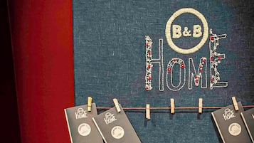 Una pared con 'B&B HOME' bordado en un estilo decorativo, mostrando varios cuadernos negros sujetos con pinzas de madera.