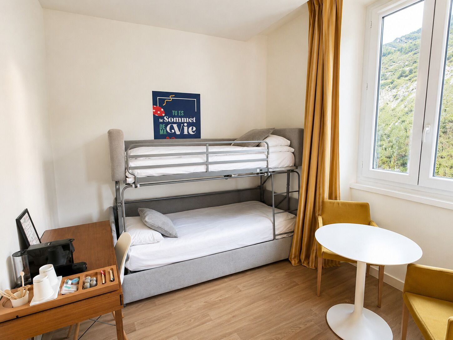 A compact room with a bunk bed, a small table with a chair, and a window with curtains.