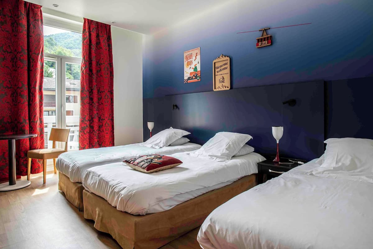 Habitación de hotel con dos camas, una silla, una mesa y vistas al exterior.
