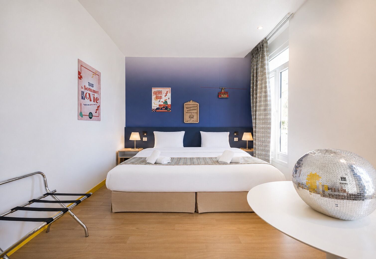 A hotel room with a large bed, bedside tables, a decorative mirror, and a poster on the wall.