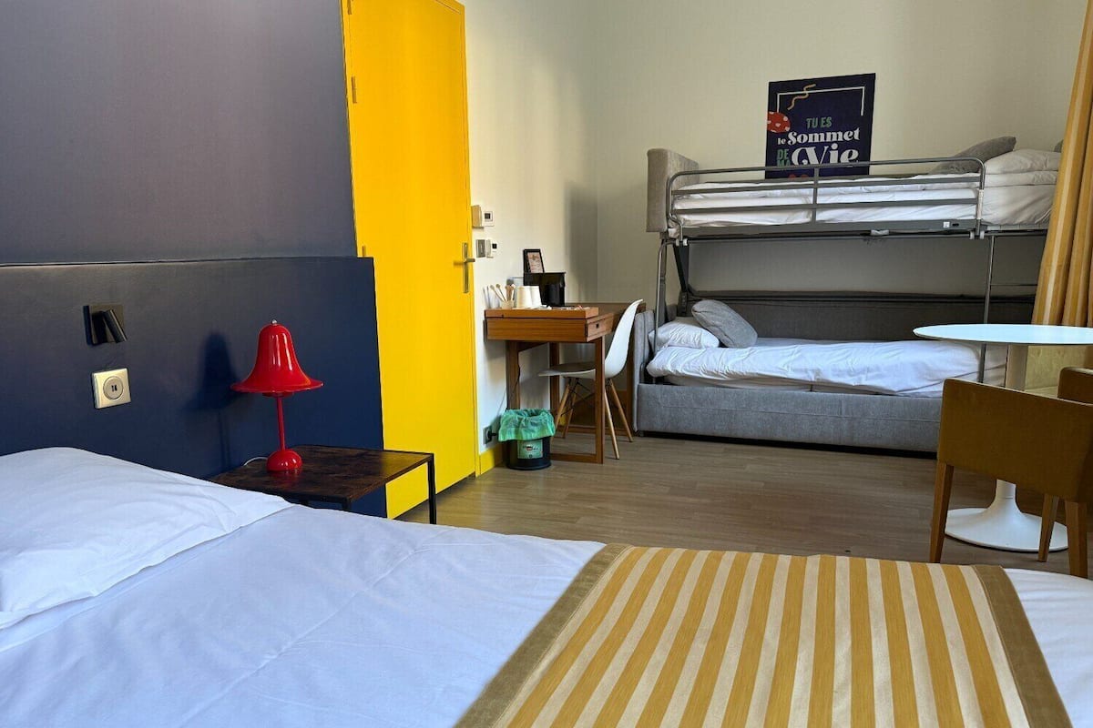 Habitación de hotel con dos camas, un escritorio, una silla y una mesita.