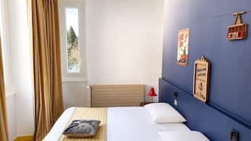 A hotel room with a bed, a window with curtains, a wall-mounted lamp, and a welcome sign.