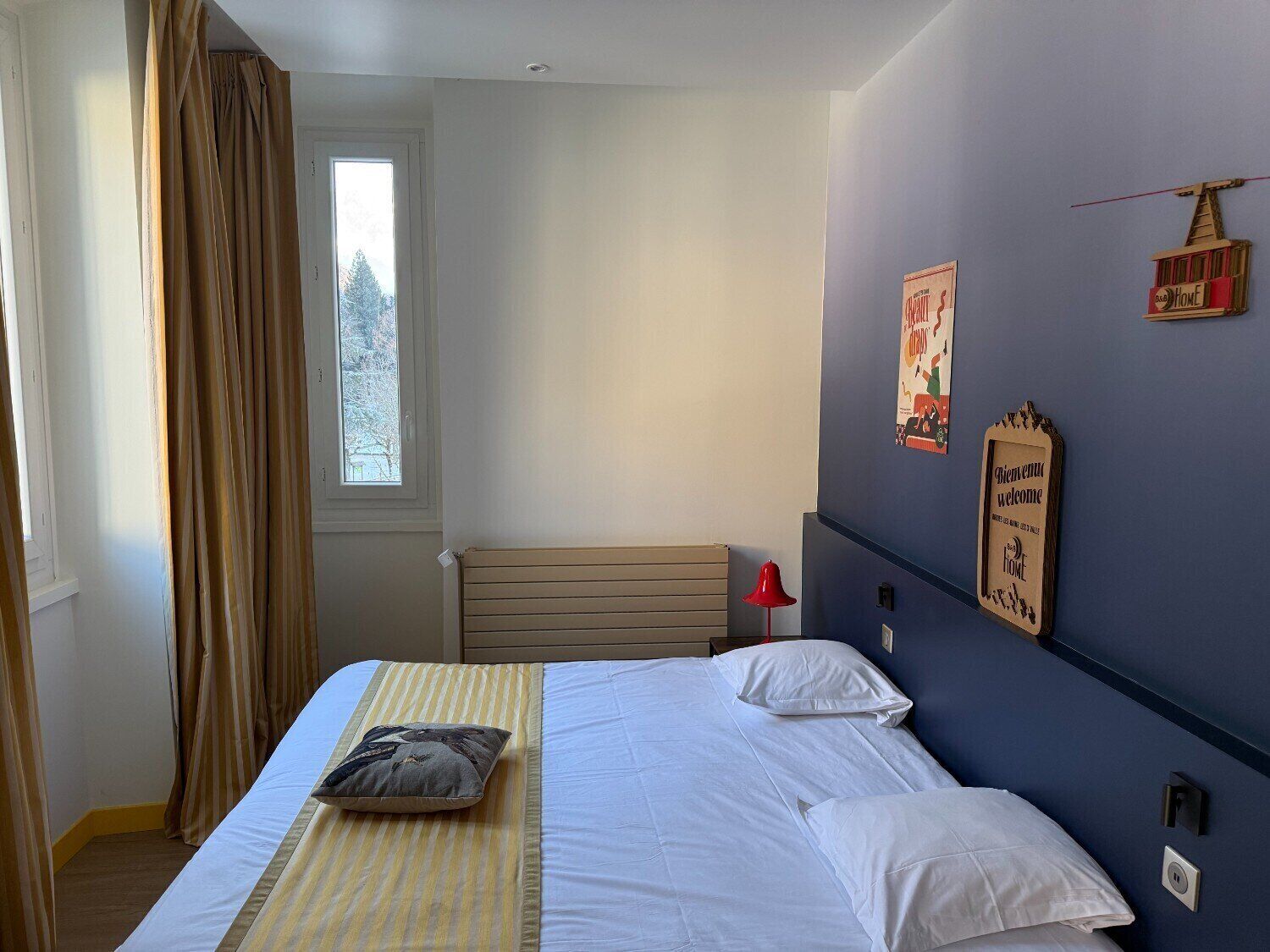 Un dormitorio con cama, ventana con cortinas, radiador y adornos en la pared.