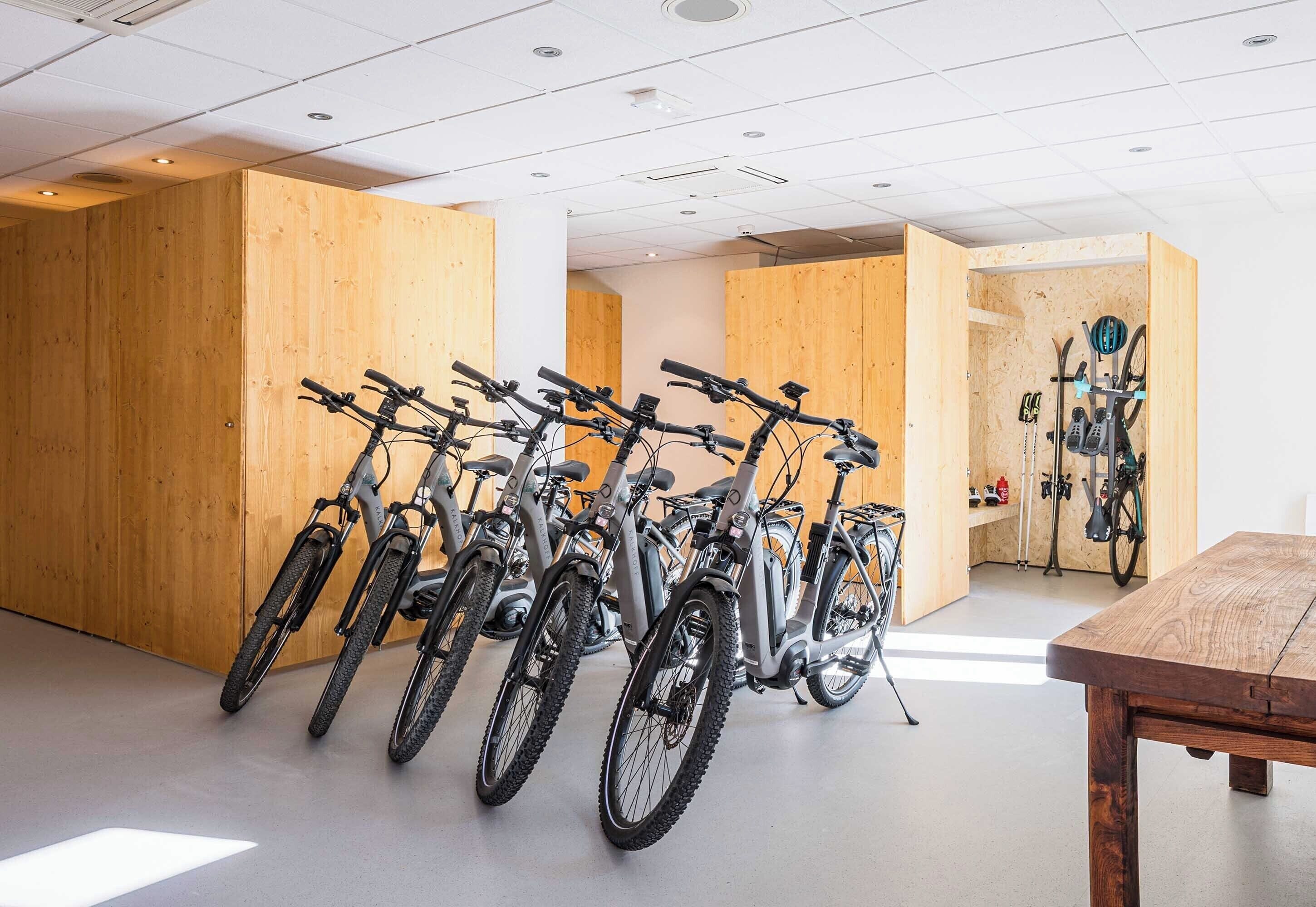 Una habitación con varias bicicletas estacionadas junto a paredes de madera, una mesa y un soporte para esquíes con esquíes y bastones.