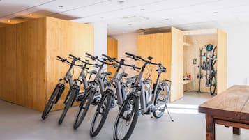 Een kamer met meerdere fietsen tegen houten wanden, een tafel en een ski-rek met ski's en stokken.