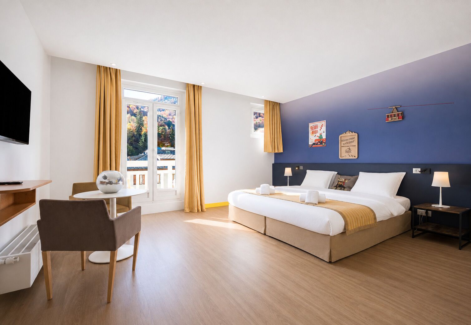 A hotel room with a bed, bedside tables, a desk, a chair, and a television.