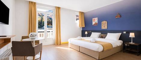 A hotel room with a bed, bedside tables, a desk, a chair, and a television.