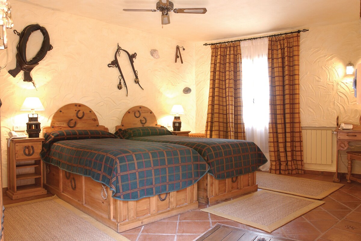 A bedroom with two wooden beds, a ceiling fan, a nightstand with a lamp, and a window with curtains.