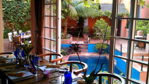 A dining area with a pool view, featuring a table set with blue glassware, a candle, and a vase with a plant. - Amanhavis Hotel (Benahavis)