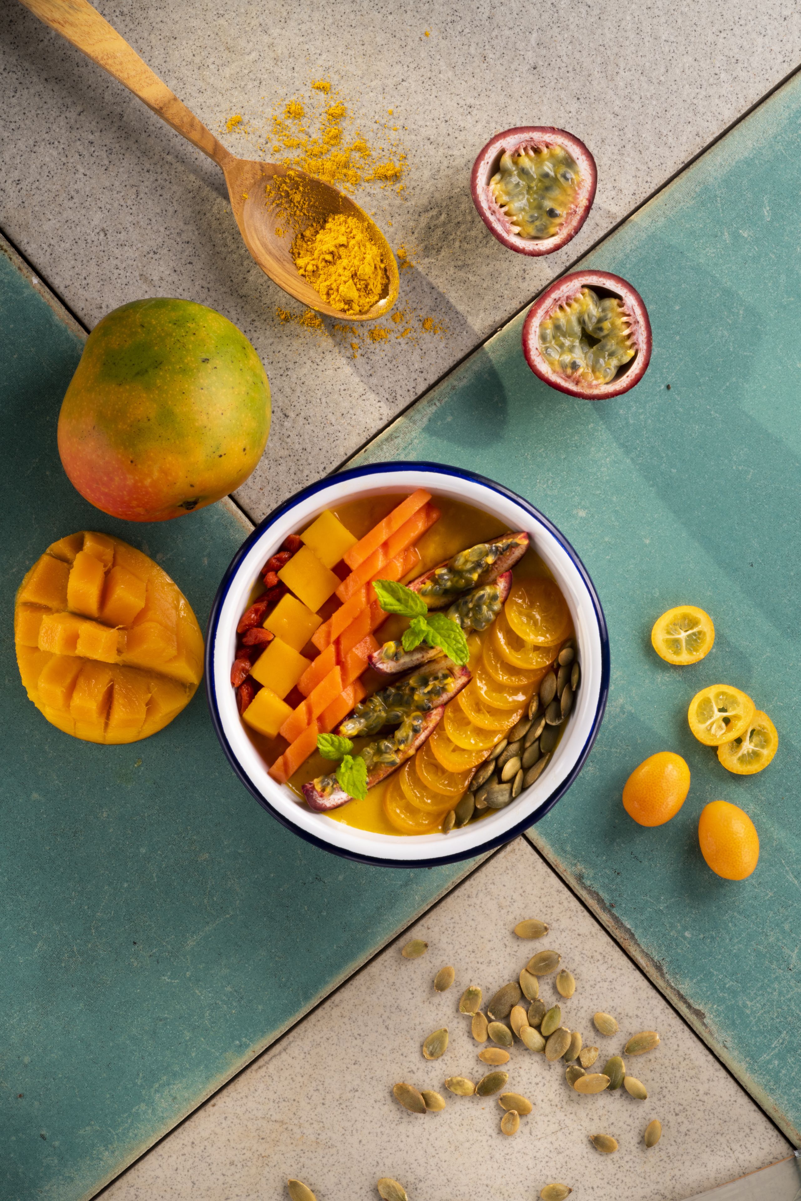 A bowl of fruit salad with mango, passion fruit, and orange slices on a teal surface.