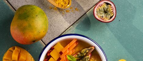 Un tazón de ensalada de frutas con mango, maracuyá y rodajas de naranja sobre una superficie color turquesa.