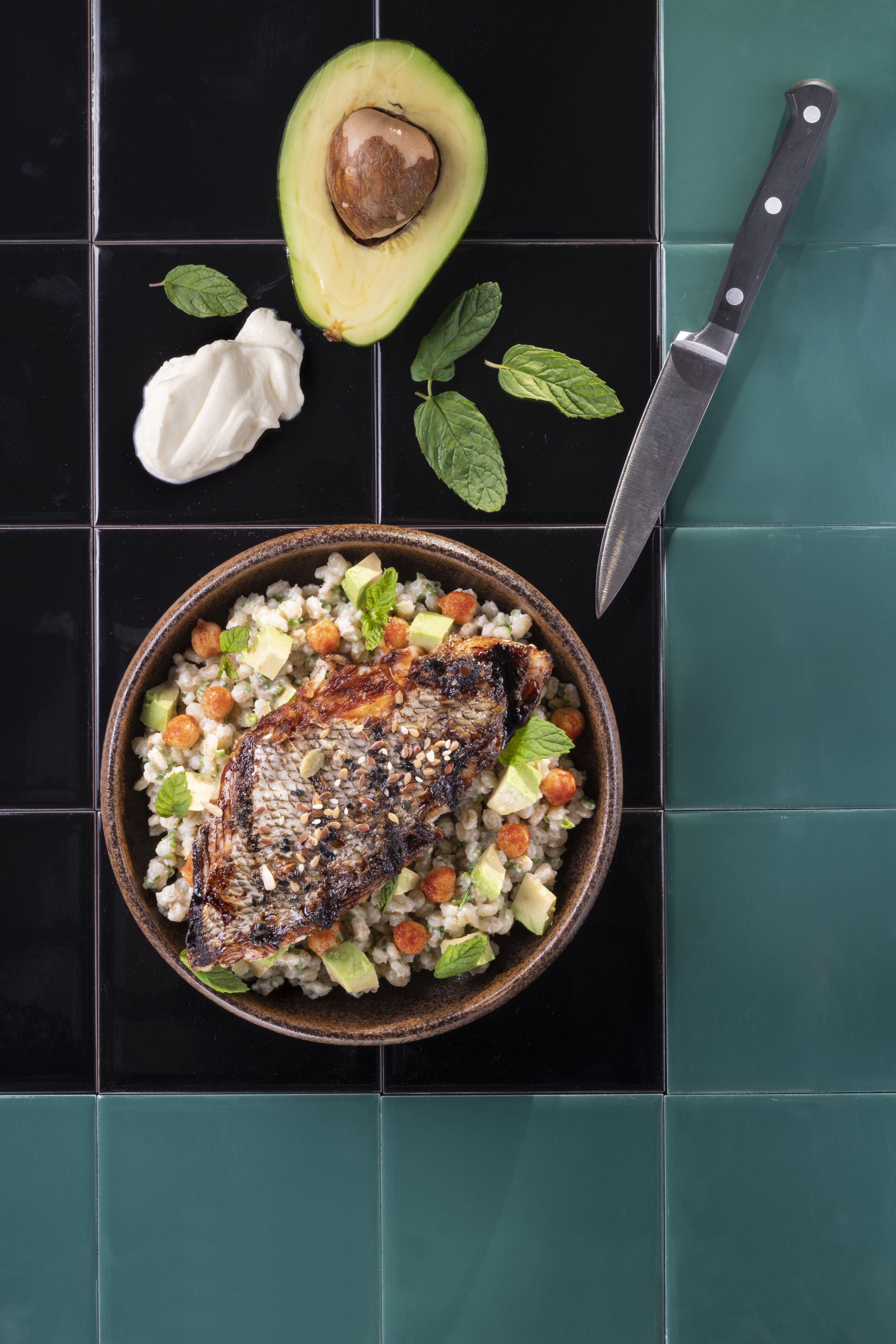 A bowl of food with a steak and vegetables on a black tiled surface.