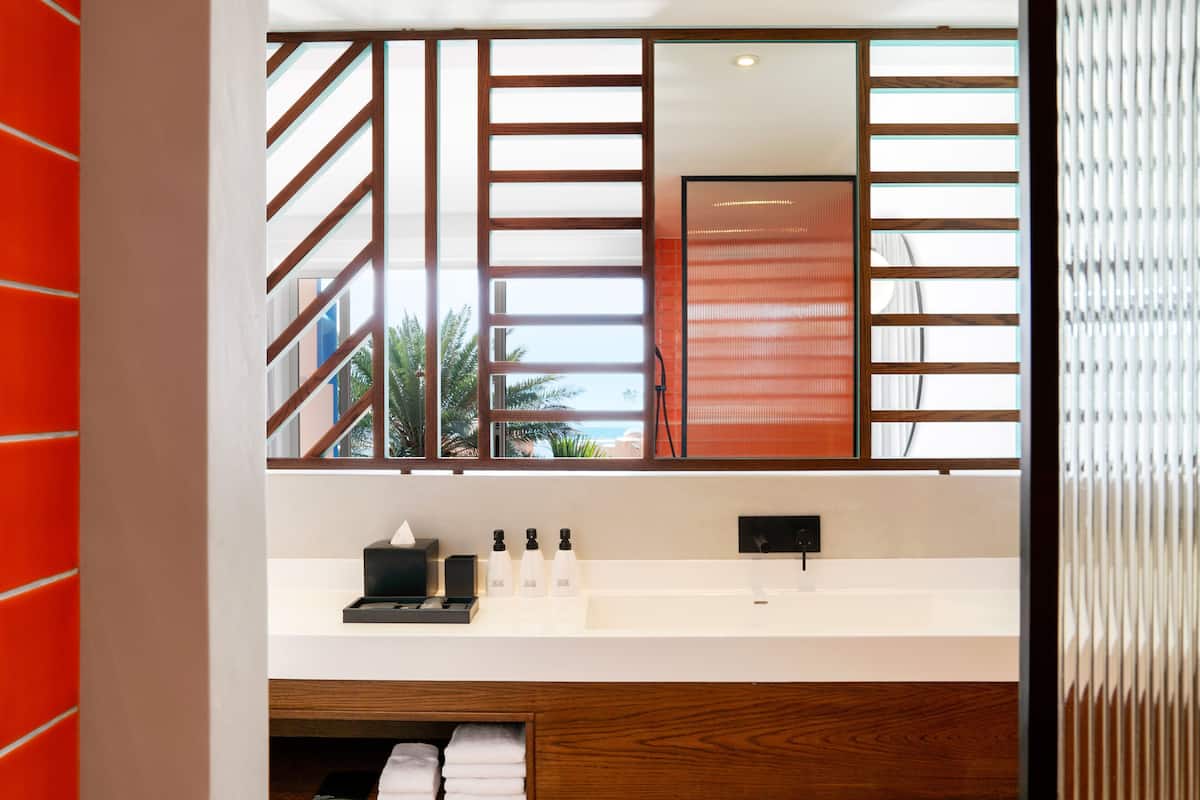 A modern bathroom with a large mirror, wooden accents, and a view of palm trees.