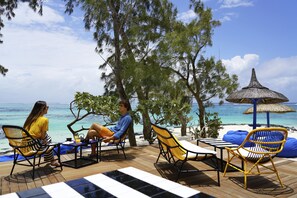 A wooden deck with outdoor seating, overlooking a beach with clear blue water and a thatched umbrella. - SALT of Palmar, an adult-only boutique Hotel (Belle Mare)