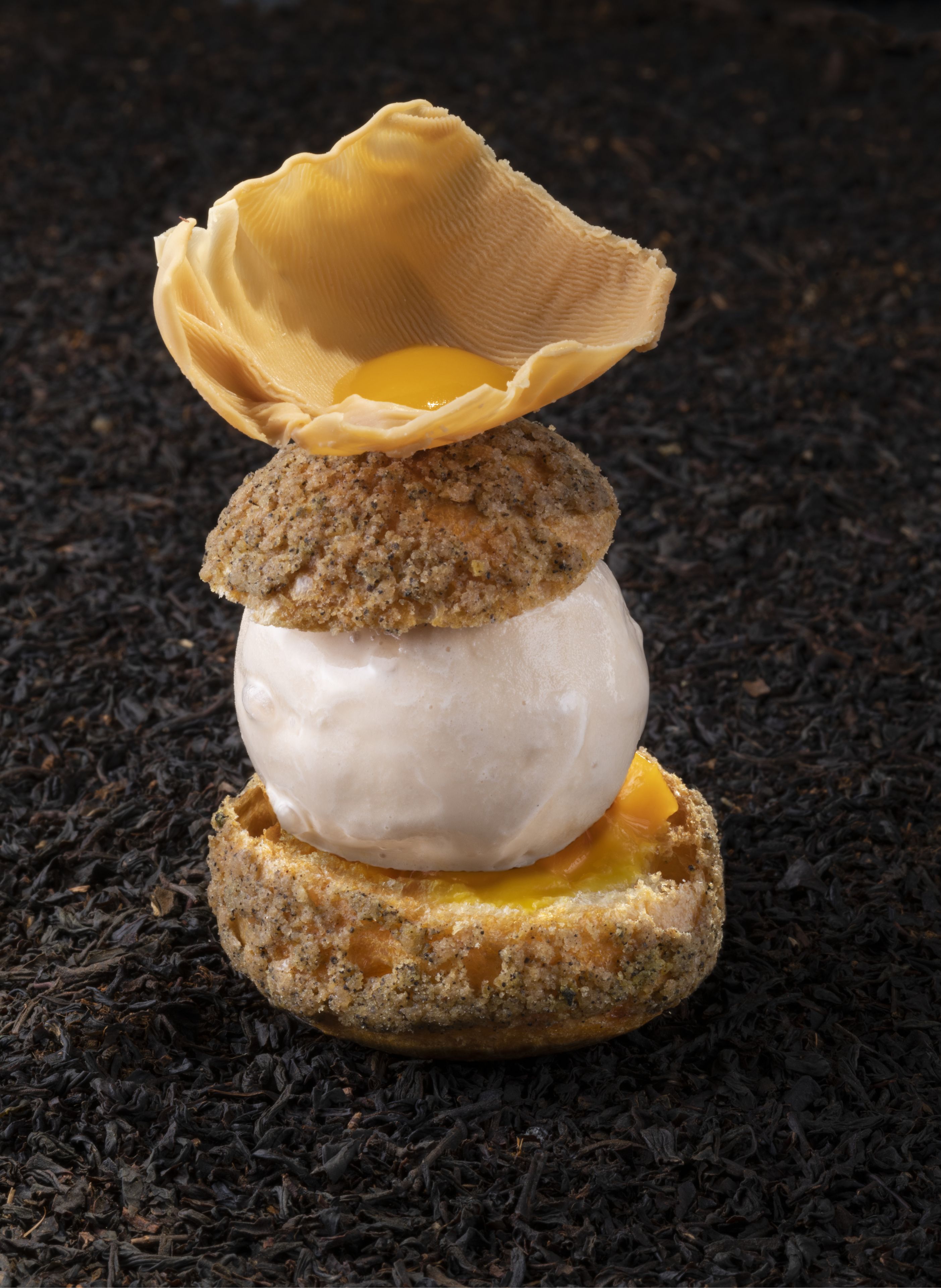 Un postre en capas con centro de crema batida, una capa intermedia de textura desmenuzable y una base de relleno amarillo, todo sobre una superficie oscura y con textura.