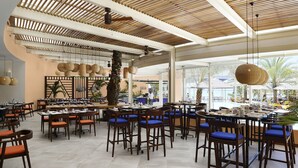 A spacious dining area with multiple tables and chairs, a high ceiling with wooden beams, and large windows offering views of the outdoors. - SALT of Palmar, an adult-only boutique Hotel (Belle Mare)