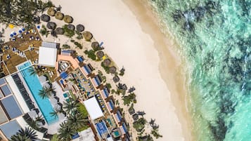 An aerial view of a beach resort with a swimming pool, sun loungers, umbrellas, and a beach area.