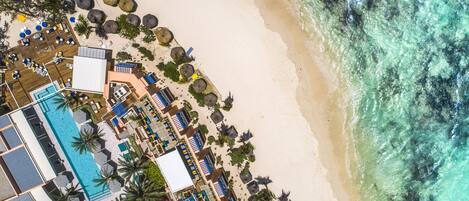 Vista aérea de un complejo turístico con piscina, tumbonas, sombrillas y una zona de playa.