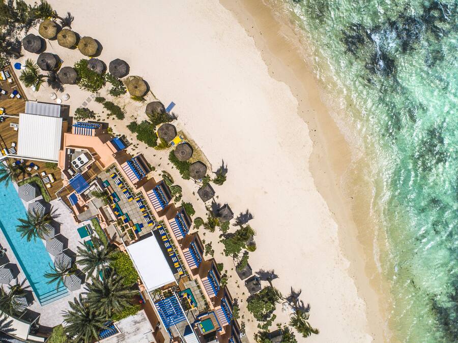 An aerial view of a beach resort with a swimming pool, sun loungers, umbrellas, and a beach area.