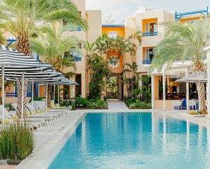 A pool area with lounge chairs and umbrellas, surrounded by palm trees and a building with balconies. - SALT of Palmar, an adult-only boutique Hotel (Belle Mare)