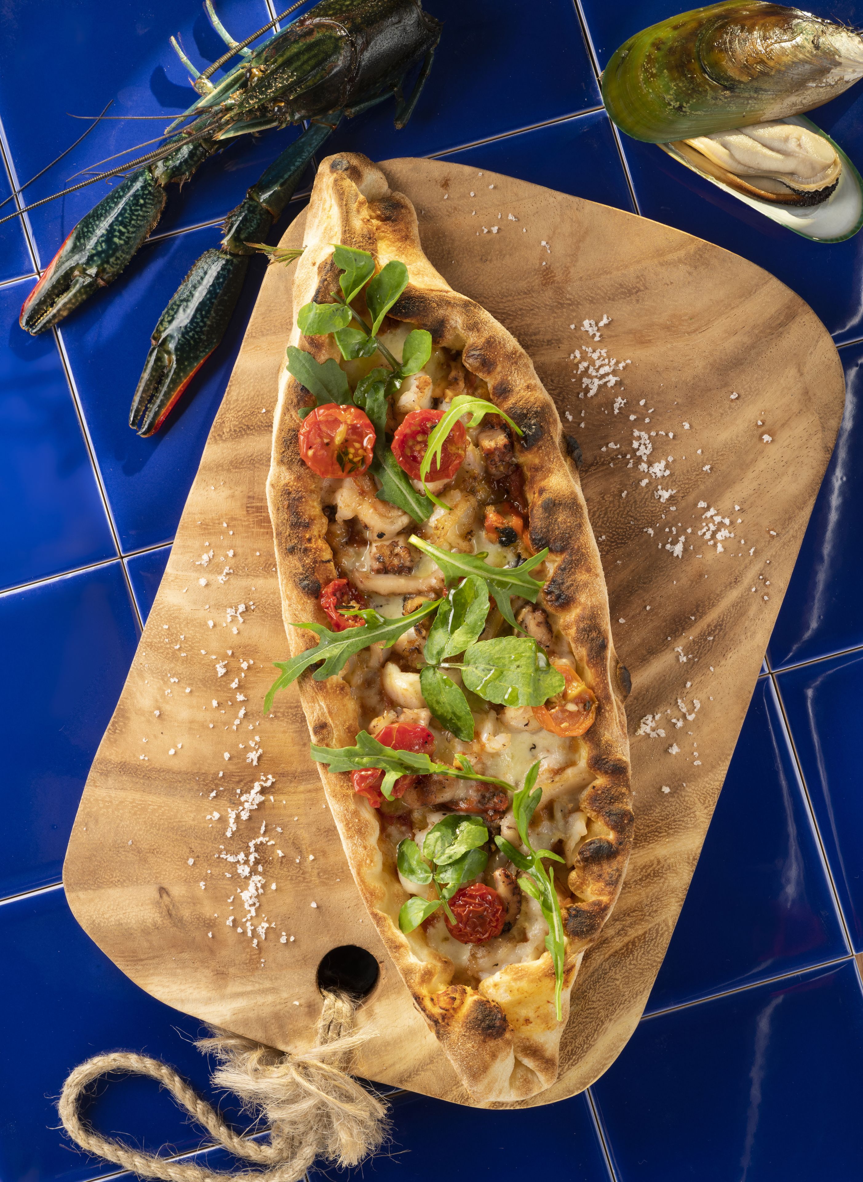 A pizza on a wooden board with a hole in the center, surrounded by vegetables and cheese.