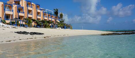 Een hotel aan het strand met helderblauw water, wit zand en gebouwen met blauwe omlijstingen.