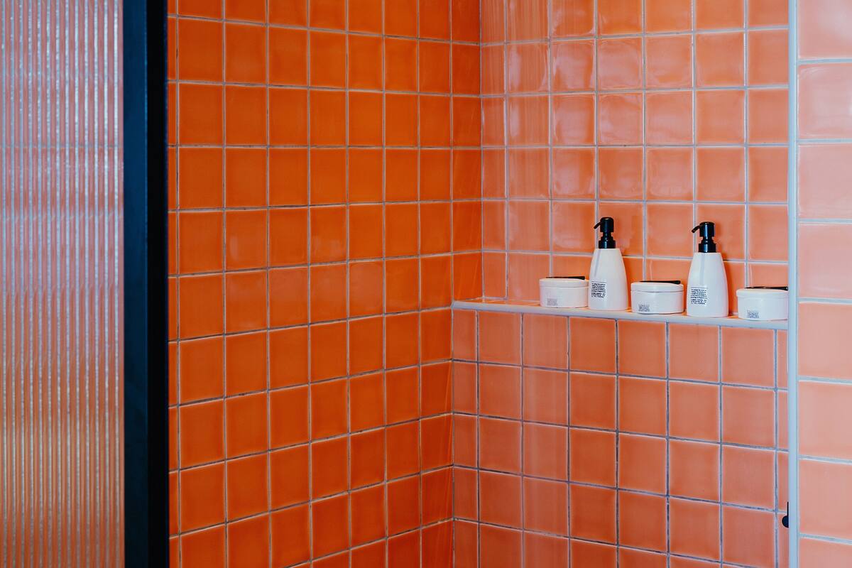 A bathroom with orange tiled walls and a white shelf holding toiletries.