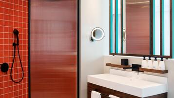 Un baño moderno con cabina de ducha de vidrio, un lavabo blanco con mueble de madera y un espejo con detalles azul turquesa.