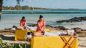 A beachside spa setup with two massage tables, a wooden table with bottles, and a clear view of the ocean and beach in the background. - SALT of Palmar, an adult-only boutique Hotel (Belle Mare)