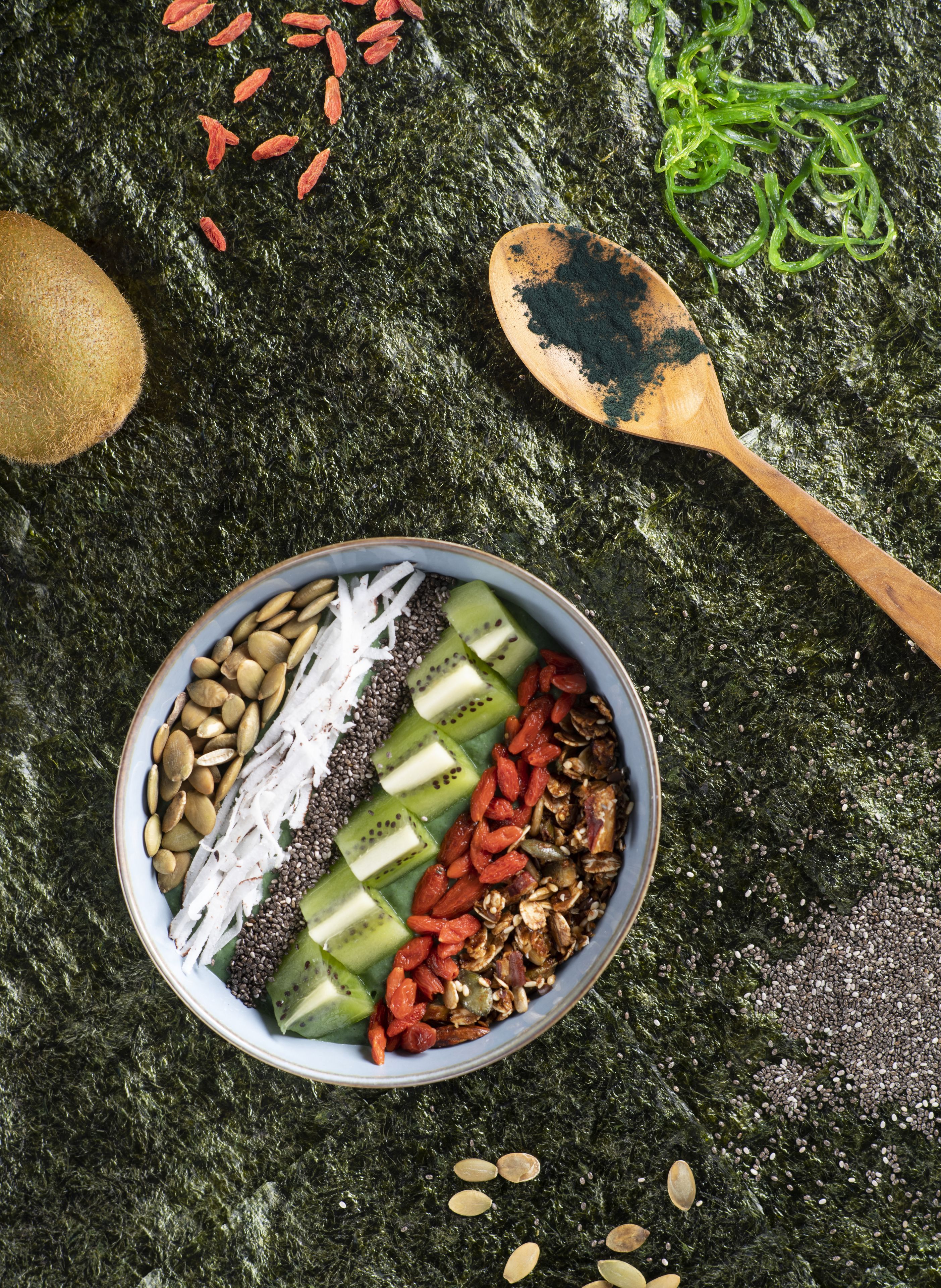 Un tazón con mezcla de nueces, semillas y frutas deshidratadas sobre una superficie rugosa.