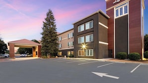 A hotel with a modern design, featuring a prominent 'La Quinta' sign, a covered parking area, and a large tree in front.