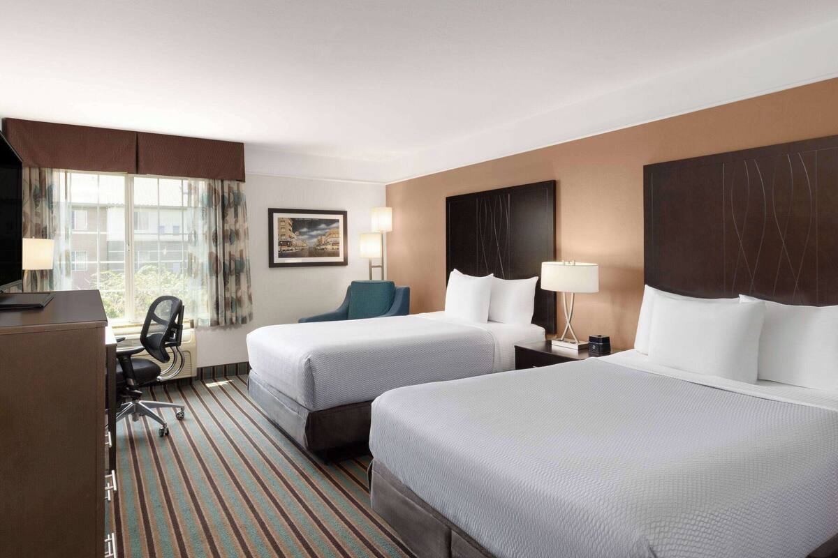 A hotel room with two beds, a desk, a chair, and a window with curtains.