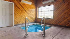 A wooden interior with a pool, metal pool ladders, and a large window.