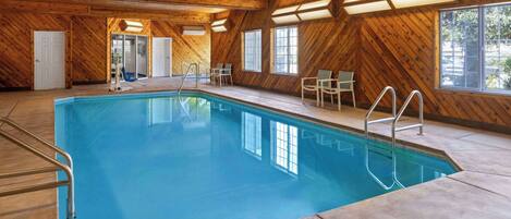 An indoor swimming pool with wooden walls and ceiling, clear glass doors, and a tiled floor.