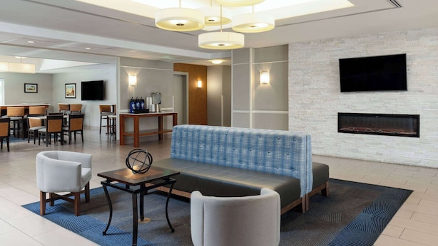 A modern hotel lobby with a seating area, a fireplace, and a dining area.