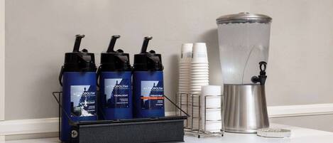 A coffee station with three coffee dispensers, a coffee pot, and several disposable cups.