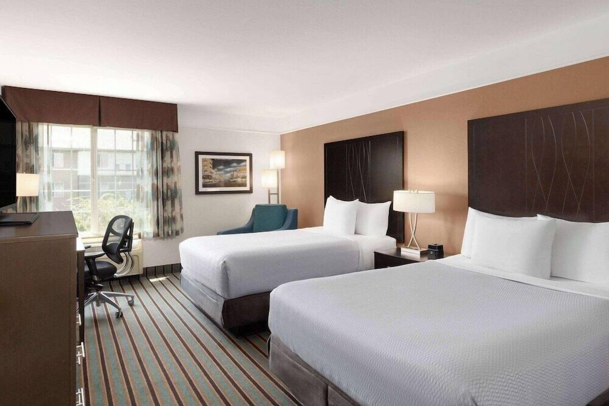 A hotel room with two beds, a desk, a chair, and a TV.
